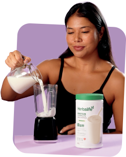 Mulher despejando leite no liquidificador ao lado do pote de Protein Complete